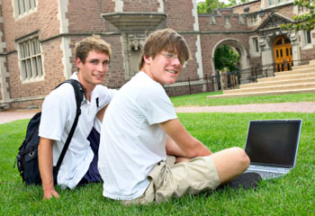 Two students sitting on grass with a laptop
